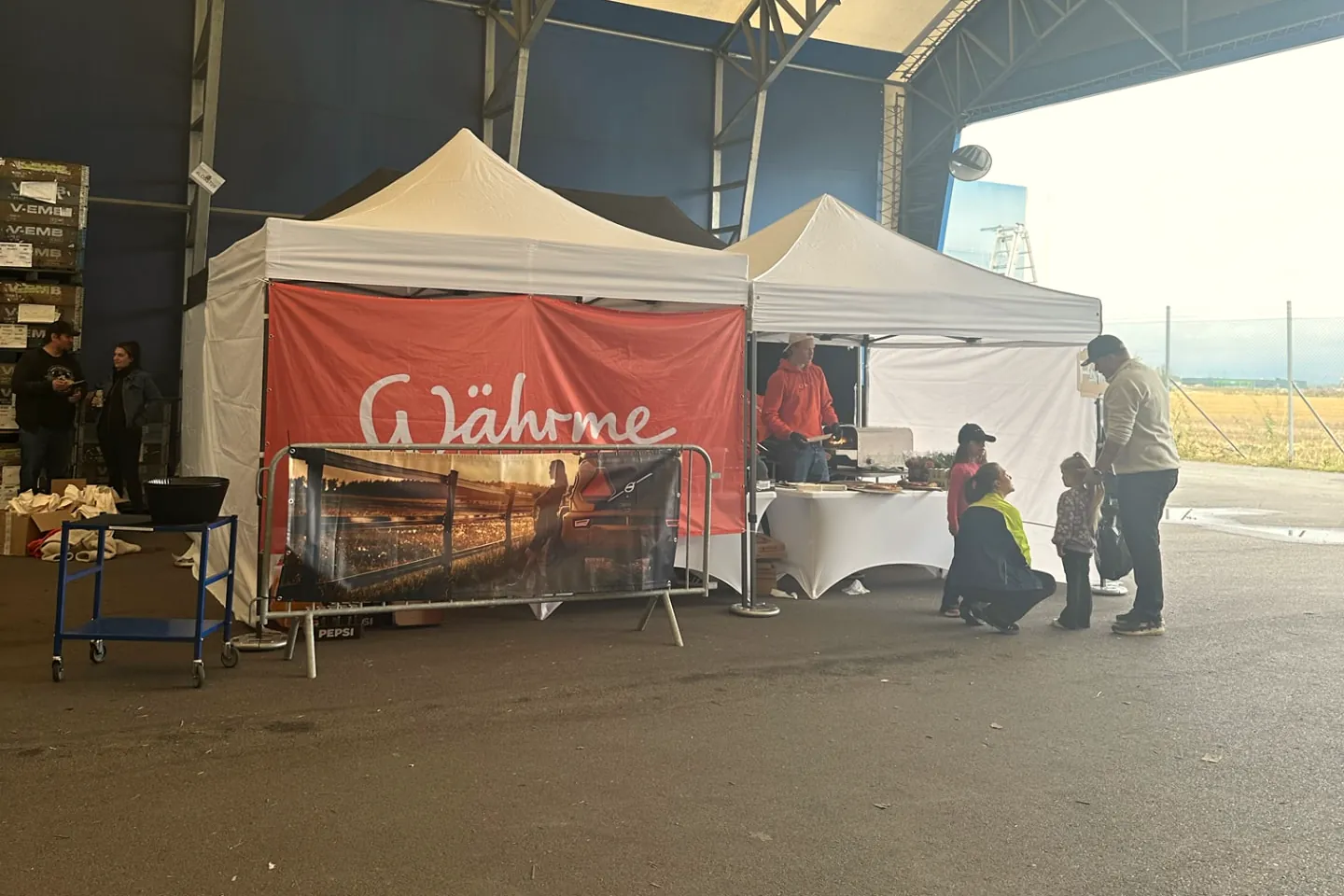 Währmes cateringtält med orange banderoll i en stor hall, med gäster vid serveringen.
